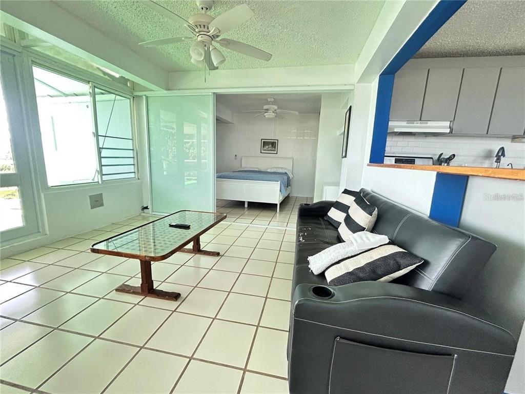 A living area with tile floors and a black sofa opens into a bedroom space — 111 FIDENCIO DE JESUS, FAJARDO, PR