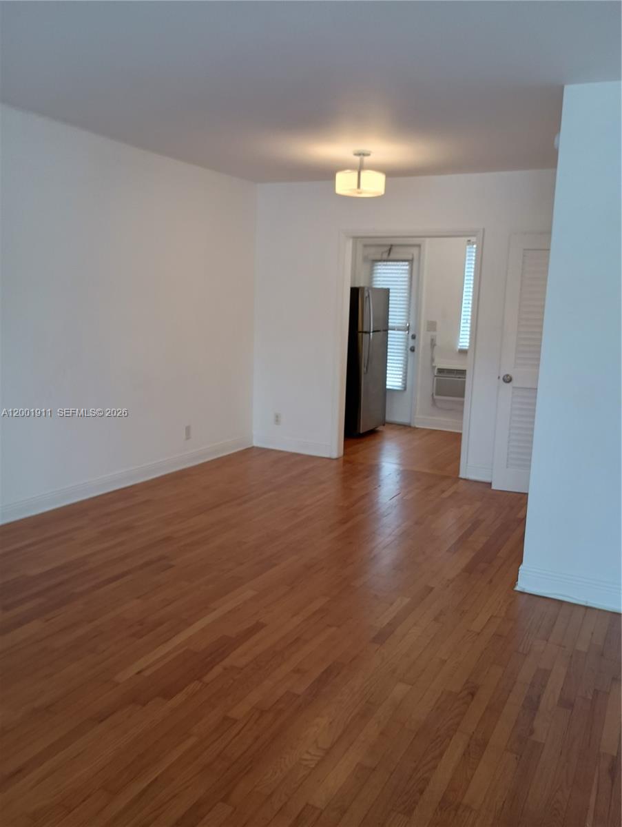 An empty room with hardwood floors leads to a kitchen area through a doorway — 535 74 # 11, Miami Beach FL 33141, MIAMI BEACH, FL
