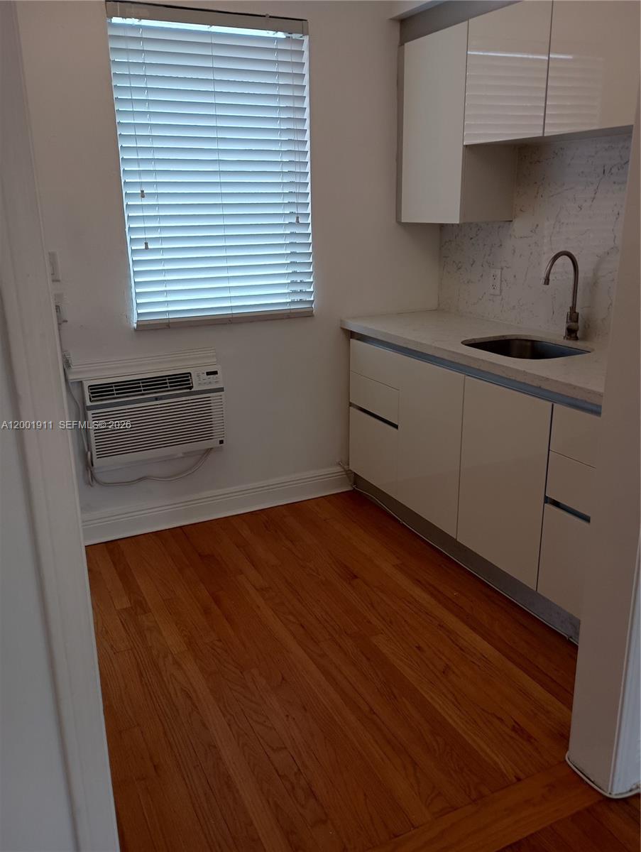 A small kitchen features white cabinets, a stainless steel sink, and hardwood flooring — 535 74 # 11, Miami Beach FL 33141, MIAMI BEACH, FL