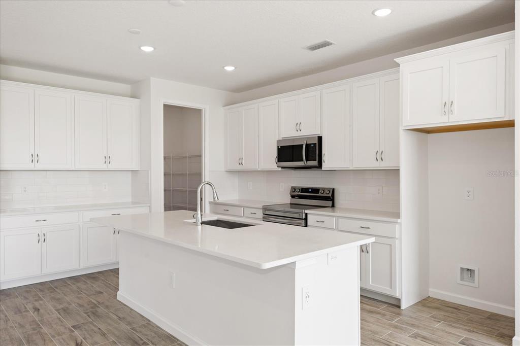 A modern kitchen features white cabinetry, a large center island, and stainless steel appliances — 9584 VIBRANT LANE, VENICE, FL