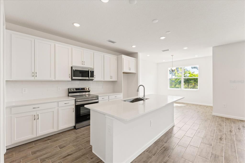 A modern kitchen features white cabinetry, a central island, stainless steel appliances, and wood-look flooring — 9584 VIBRANT LANE, VENICE, FL