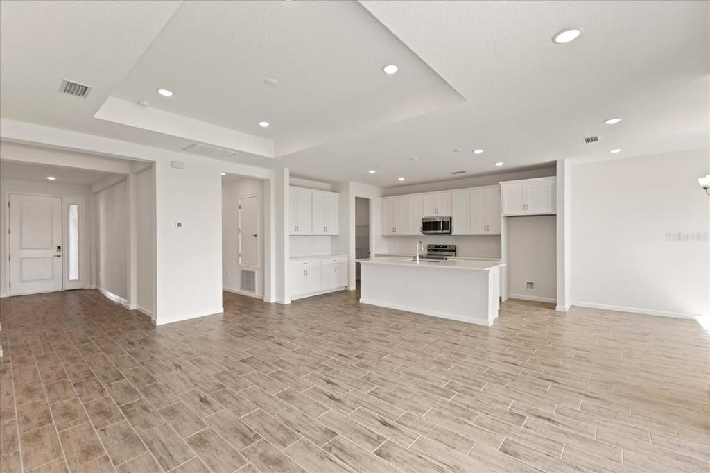 An open-concept kitchen and living area featuring white cabinetry, a center island, and tile flooring — 9584 VIBRANT LANE, VENICE, FL