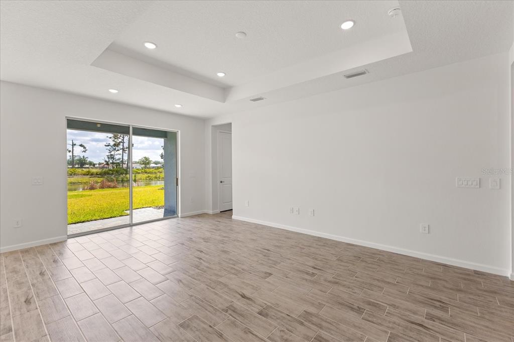 An empty living room features wood-look tile flooring, a tray ceiling, and sliding glass doors — 9584 VIBRANT LANE, VENICE, FL