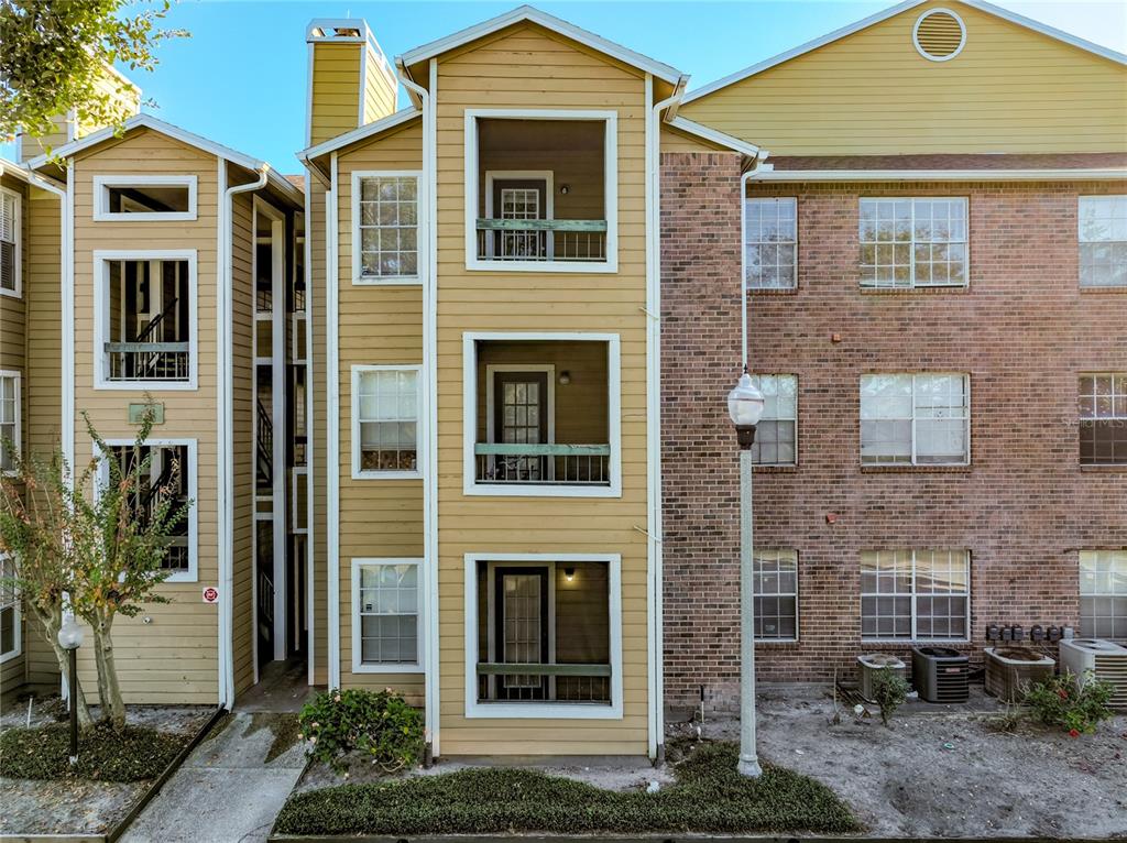 A three-story apartment building exterior featuring tan siding, brick accents, and screened-in balconies — 4301 LIZSHIRE LANE UNIT 107, ORLANDO, FL