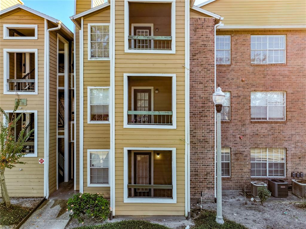 A three-story apartment building exterior features tan siding, brick accents, and screened-in balconies — 4301 LIZSHIRE LANE UNIT 107, ORLANDO, FL