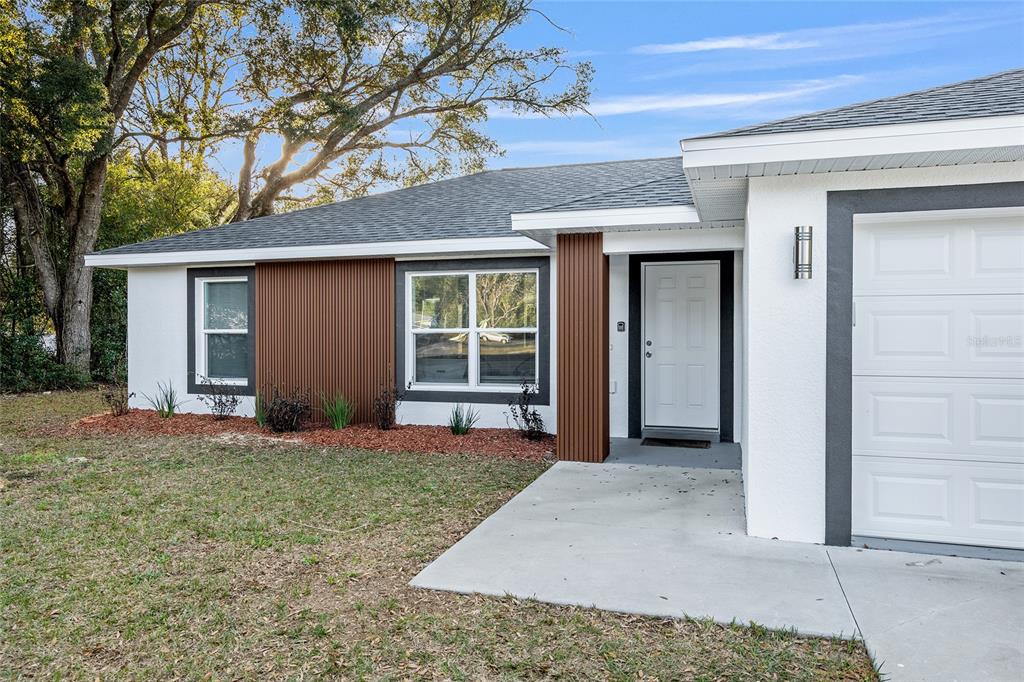 A single-story house exterior features white stucco walls, vertical brown wood siding, and a garage — 7778 SW 146TH LANE ROAD, OCALA, FL