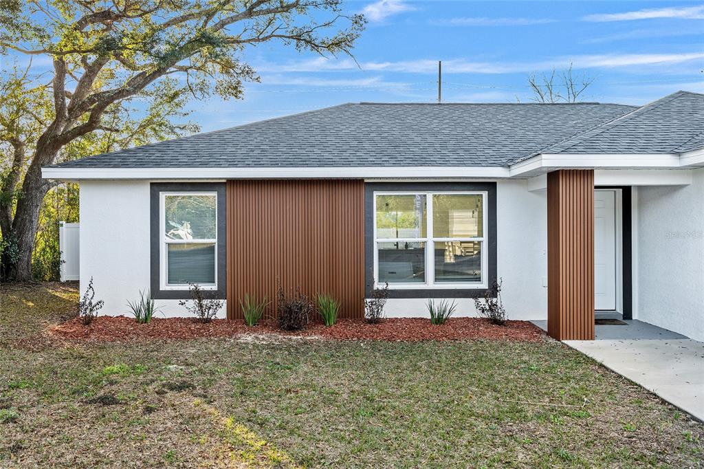 A white house exterior features vertical wood-look siding accents and a dark shingled roof — 7778 SW 146TH LANE ROAD, OCALA, FL