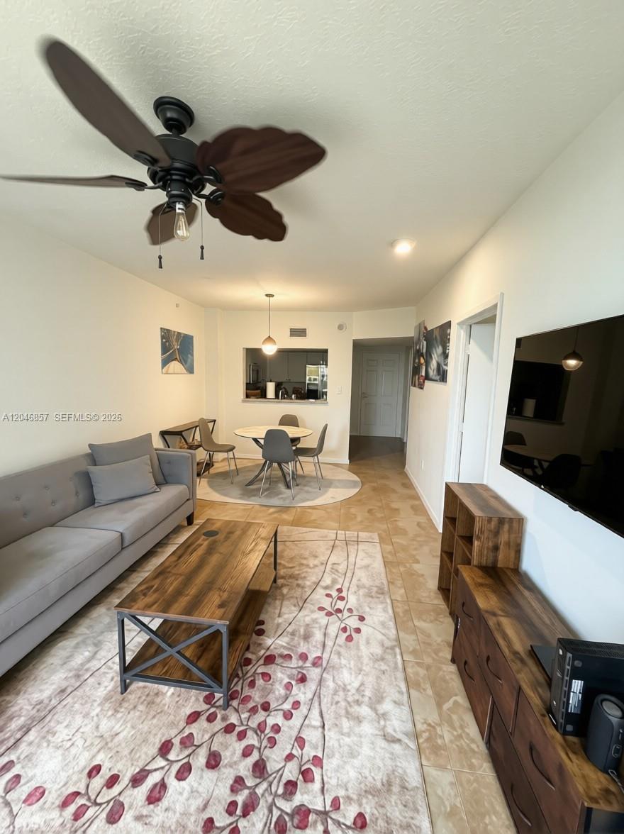 A living room with a gray sofa, wood coffee table, and dining area with tile floors — FORT LAUDERDALE, FL