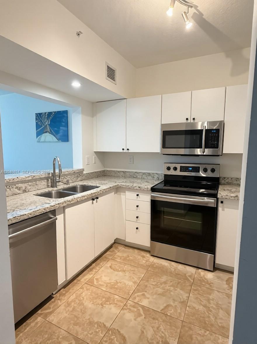 A kitchen features white cabinets, stainless steel appliances, granite countertops, and beige tile flooring — FORT LAUDERDALE, FL