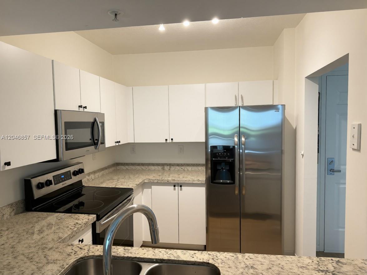 A kitchen features white cabinets, granite countertops, and stainless steel appliances — FORT LAUDERDALE, FL