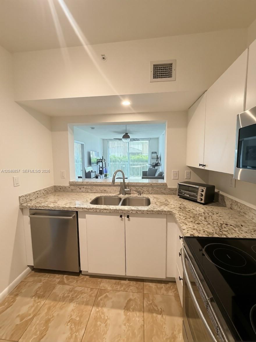A kitchen features white cabinets, granite countertops, stainless steel appliances, and a pass-through window — FORT LAUDERDALE, FL