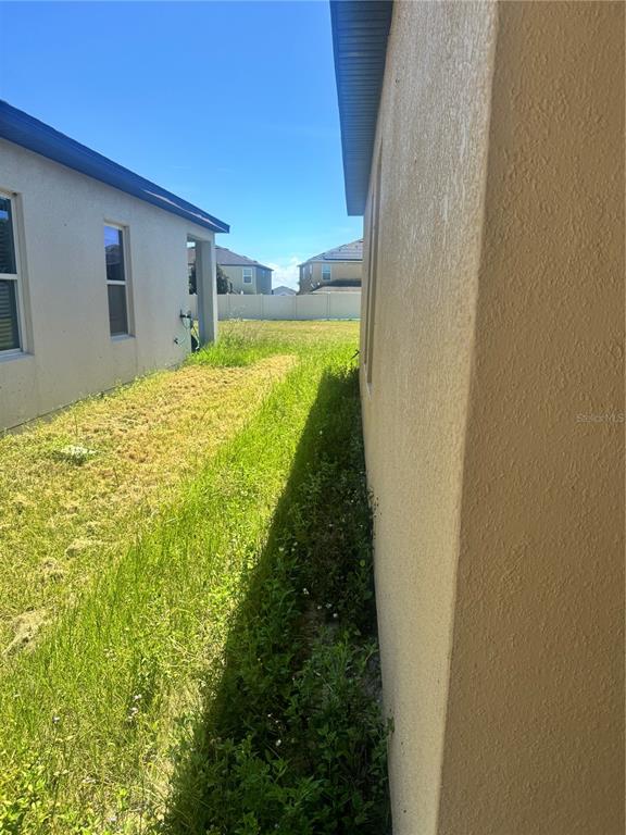 A narrow grassy side yard sits between two beige stucco houses under a clear sky — 487 EAGLECREST DRIVE, HAINES CITY, FL