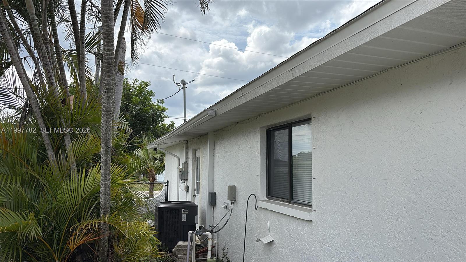 The exterior of a white stucco house features an air conditioning unit and a window — 251 SW 22 Place, Cape Coral FL 33991, CAPE CORAL, FL