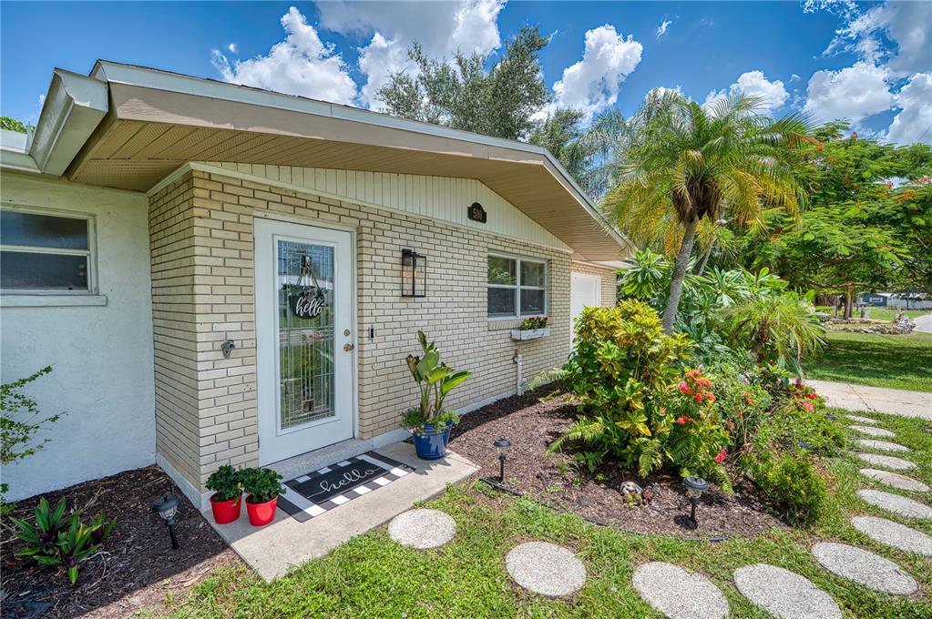 A brick house exterior features a white front door, a walkway, and landscaped garden beds — 510 DONA DRIVE, NOKOMIS, FL
