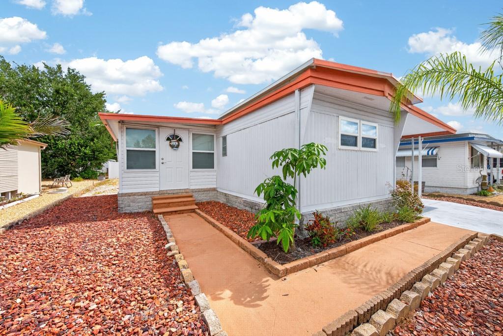 A single-story manufactured home with light gray siding, orange trim, and a concrete walkway — 3527 TIKI DRIVE, HOLIDAY, FL