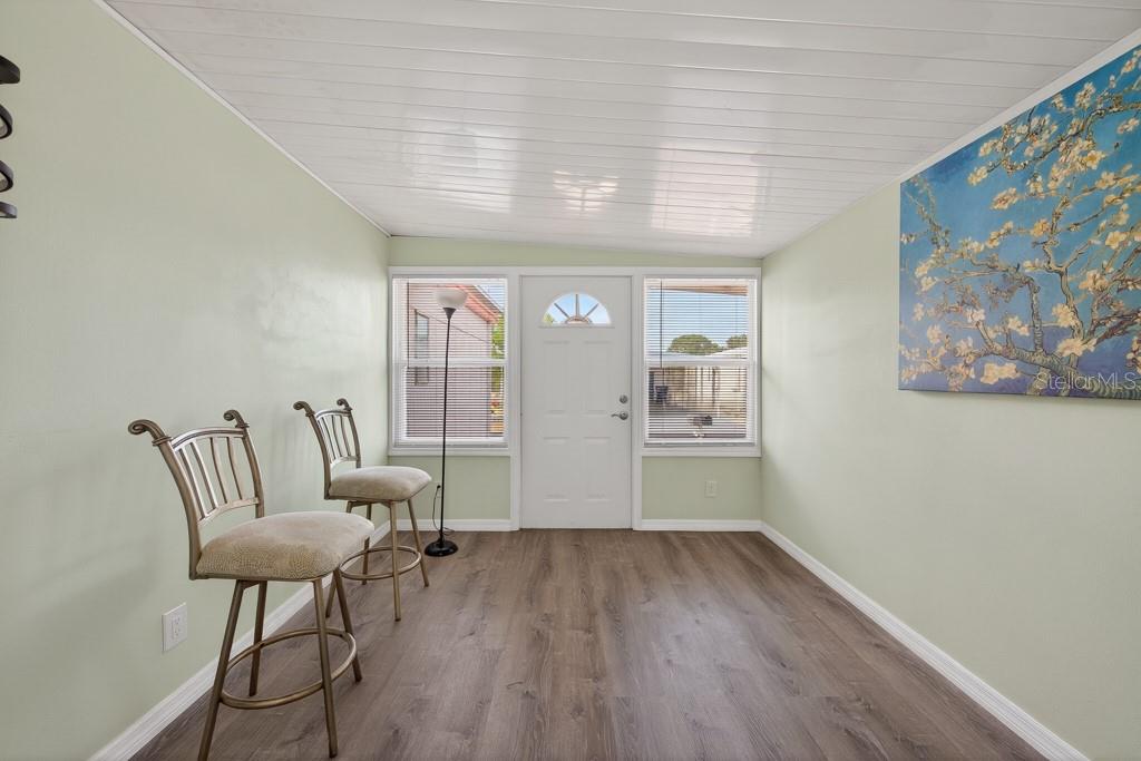 A sunroom features light green walls, wood-look flooring, two bar stools, and a white door — 3527 TIKI DRIVE, HOLIDAY, FL