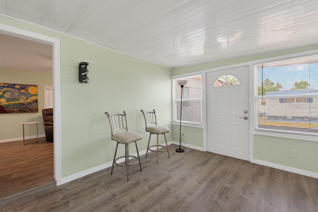 A room with light green walls, wood-look flooring, two bar stools, and a white door — 3527 TIKI DRIVE, HOLIDAY, FL