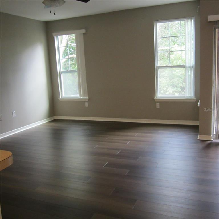 An empty room features dark wood-look flooring, gray walls, and two windows with blinds — 1985 ERVING CIRCLE UNIT 205, OCOEE, FL