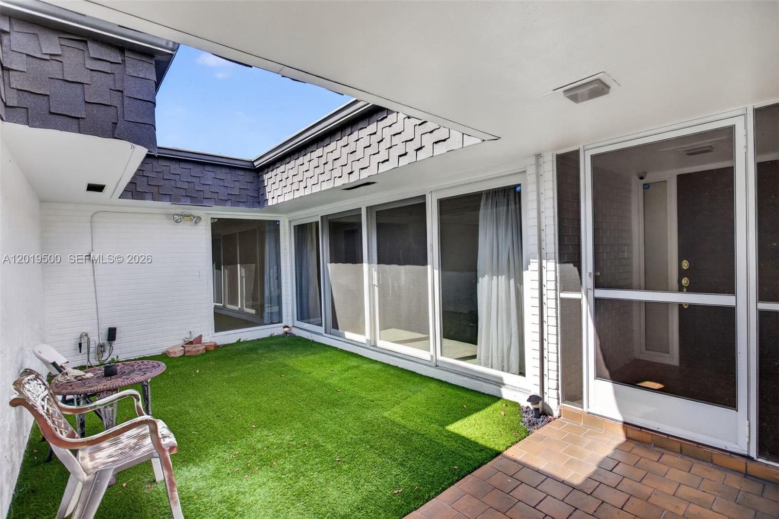 An outdoor courtyard features artificial turf, a small patio table, and large glass sliding doors — 4806 Banyan Ln, Tamarac FL 33319, TAMARAC, FL