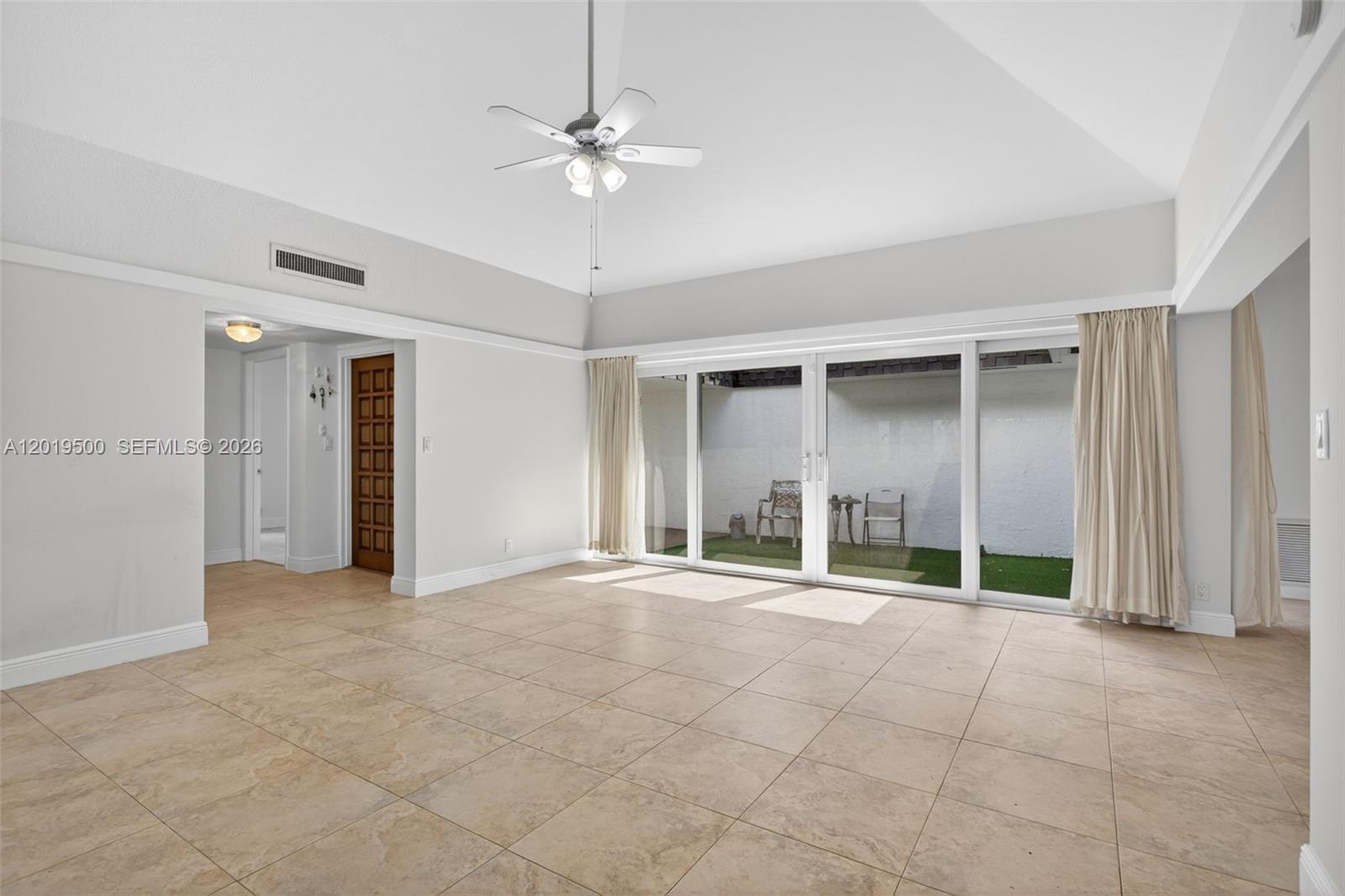 A spacious living room features light tile flooring, a vaulted ceiling, and sliding glass doors — 4806 Banyan Ln, Tamarac FL 33319, TAMARAC, FL