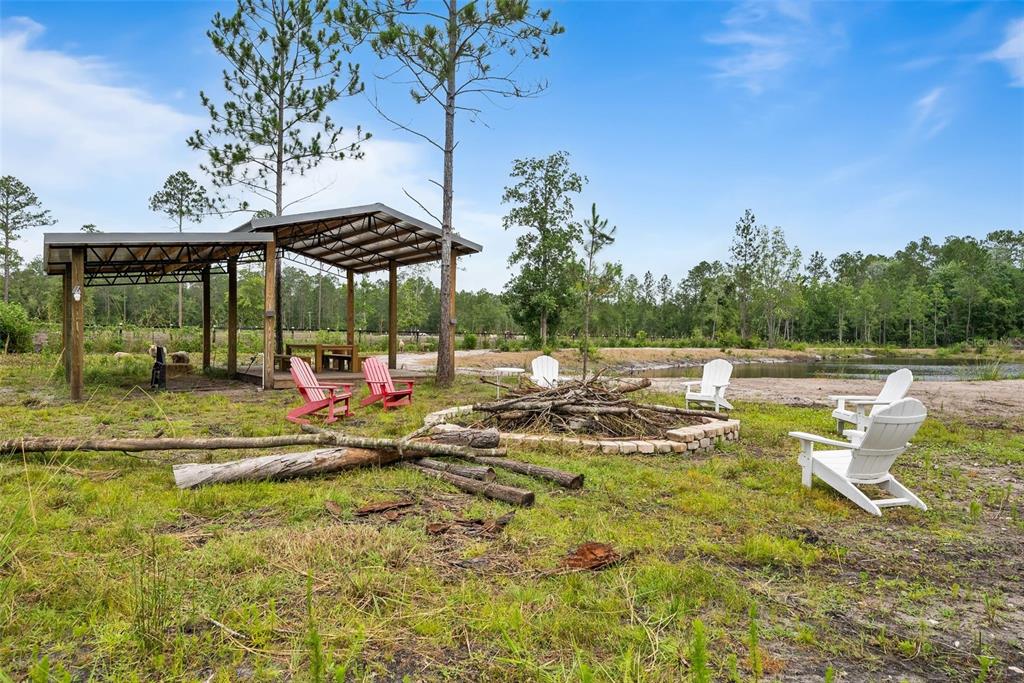 An outdoor fire pit area with Adirondack chairs sits near a covered pavilion and pond — 5753 RETREAT ROAD, KEYSTONE HEIGHTS, FL