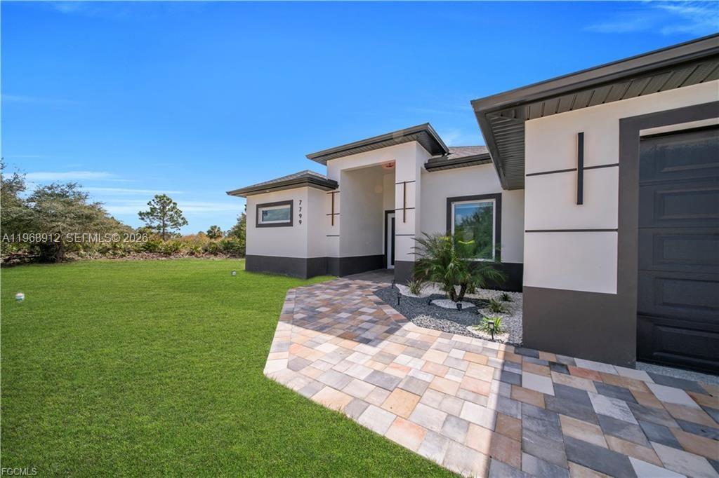 A modern single-story house exterior features a paved walkway, a small palm tree, and a garage — 7799 15th PL, La Belle FL 33935, LA BELLE, FL