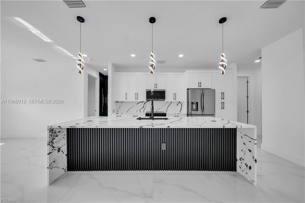A modern kitchen features a large marble-topped island with black fluted paneling and pendant lighting — 7799 15th PL, La Belle FL 33935, LA BELLE, FL