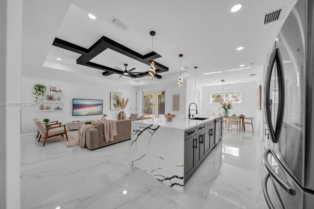 A modern open-concept kitchen and living area featuring a marble-topped island and coffered ceiling — 7799 15th PL, La Belle FL 33935, LA BELLE, FL