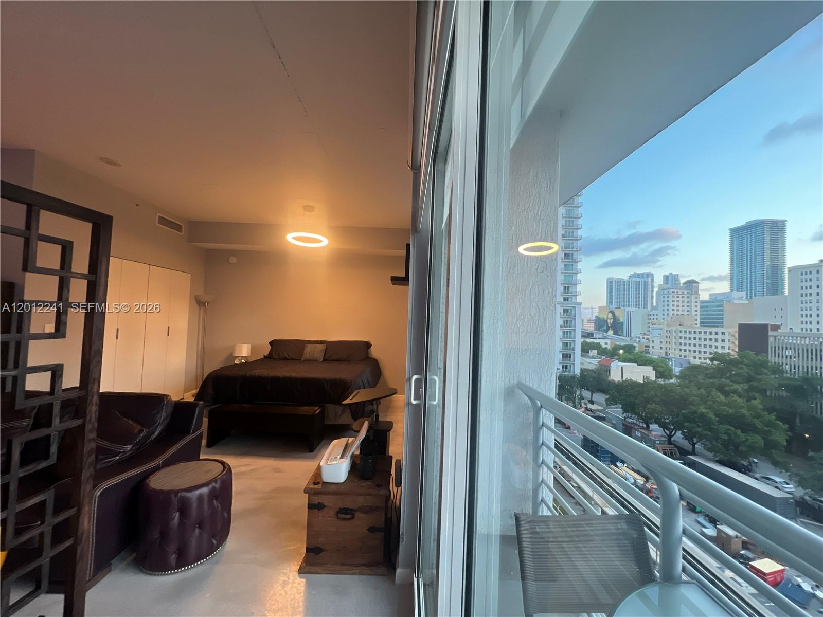 A studio apartment features a bed, living area, and a balcony overlooking a city skyline — 234 NE 3rd St # 703, Miami FL 33132, MIAMI, FL