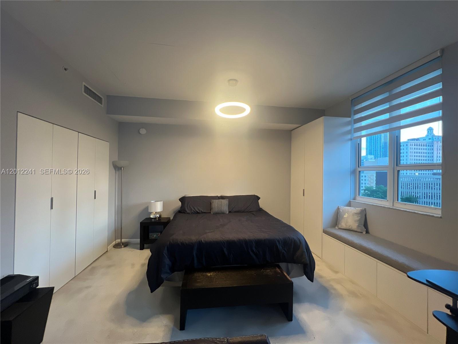 A bedroom features a bed, built-in white closets, a window seat, and a modern light fixture — 234 NE 3rd St # 703, Miami FL 33132, MIAMI, FL