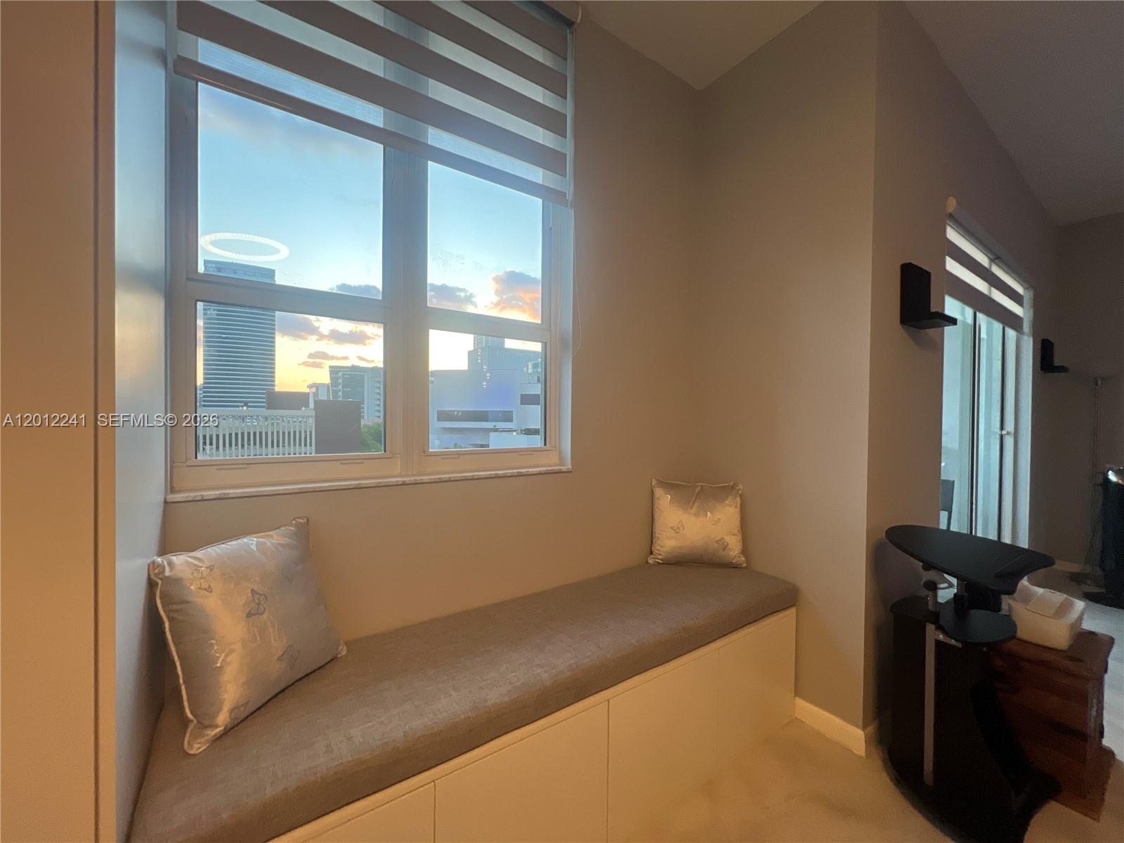 A window seat with a grey cushion and two pillows sits beneath a large window — 234 NE 3rd St # 703, Miami FL 33132, MIAMI, FL