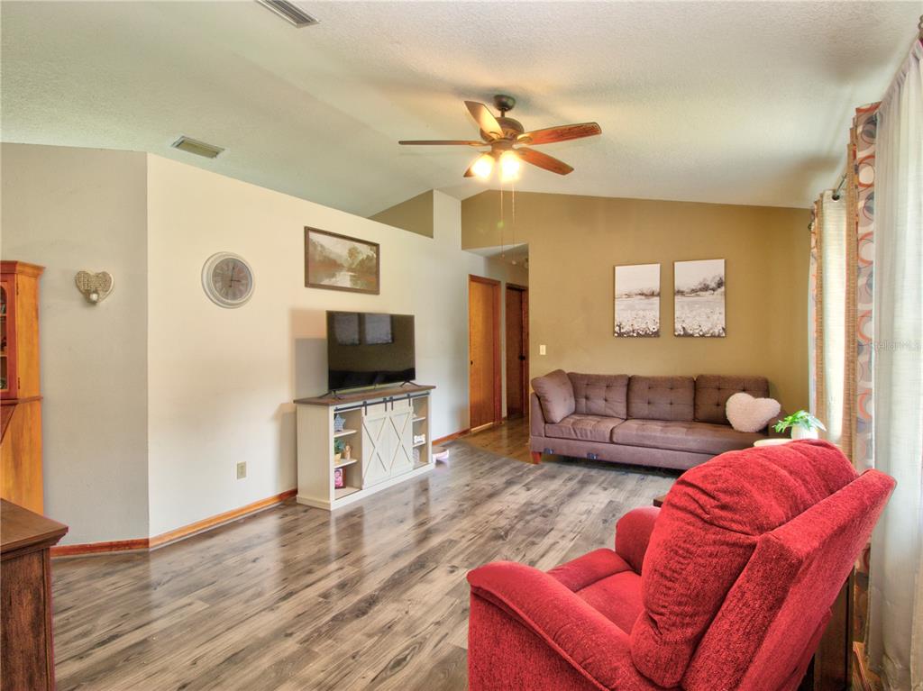 A living room features wood-look flooring, a brown sofa, a red recliner, and a television — 3815 SE 62ND STREET, OCALA, FL