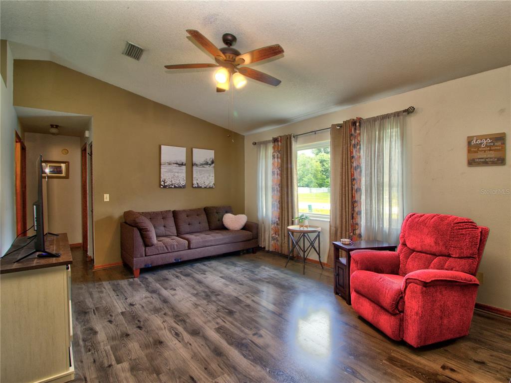 A living room features wood-look flooring, a brown sofa, a red recliner, and a ceiling fan — 3815 SE 62ND STREET, OCALA, FL