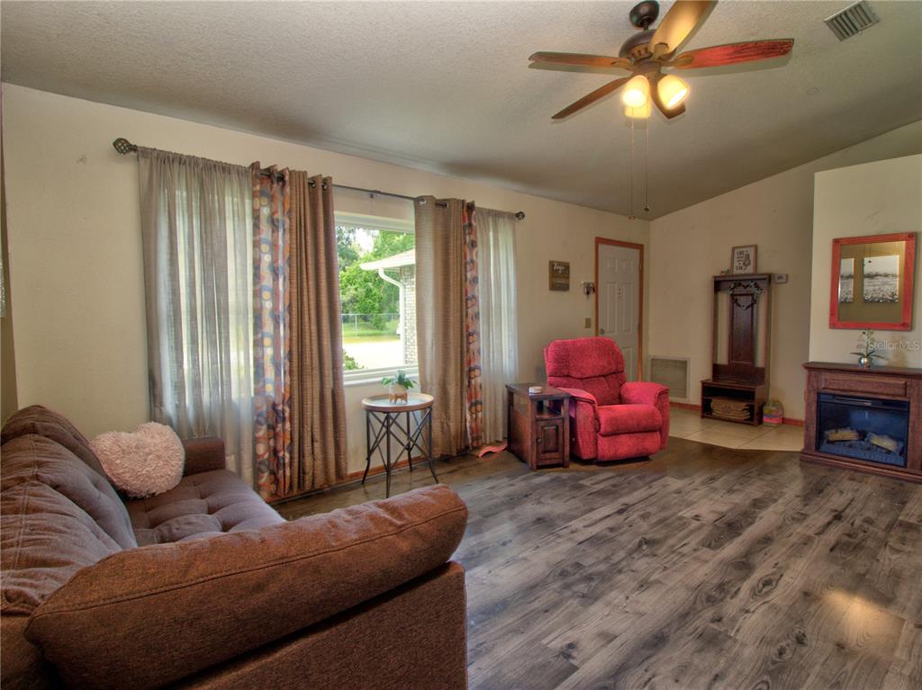 A living room features wood-look flooring, a ceiling fan, a fireplace, and a red recliner — 3815 SE 62ND STREET, OCALA, FL