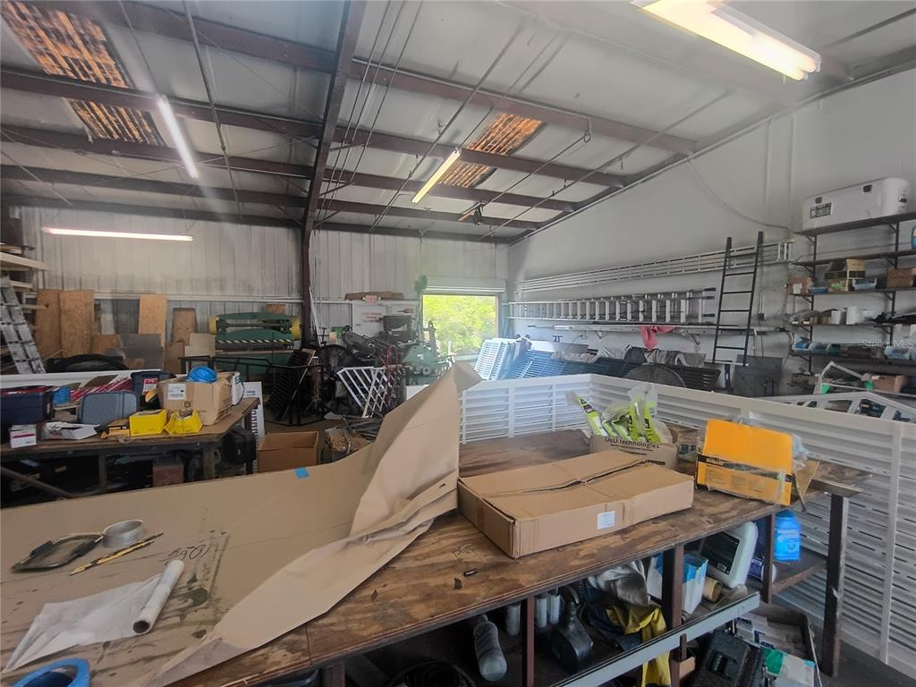 A cluttered industrial workshop features workbenches, metal shelving, and various tools under a high ceiling — 918 SE 9TH LANE, CAPE CORAL, FL