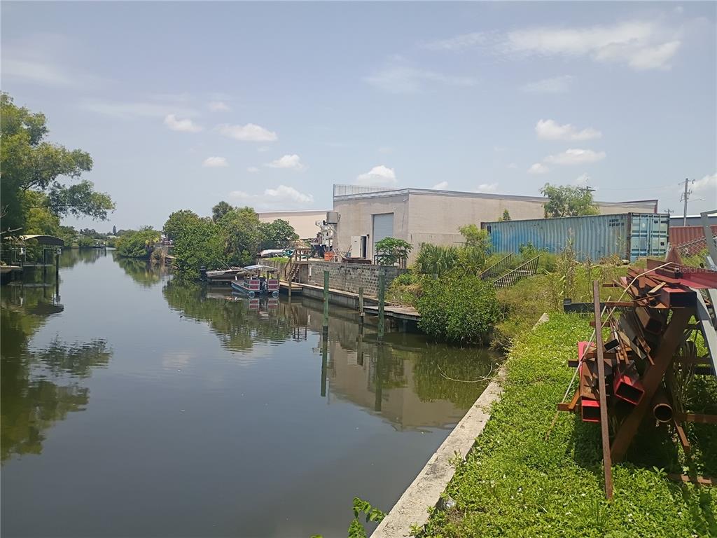 A canal view shows a concrete seawall, a metal warehouse, and a stack of steel — 918 SE 9TH LANE, CAPE CORAL, FL