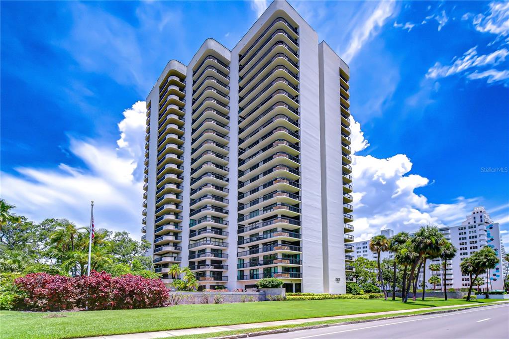 A tall, multi-story residential apartment building with many balconies stands against a bright blue sky — 2413 BAYSHORE BOULEVARD UNIT 1903, TAMPA, FL