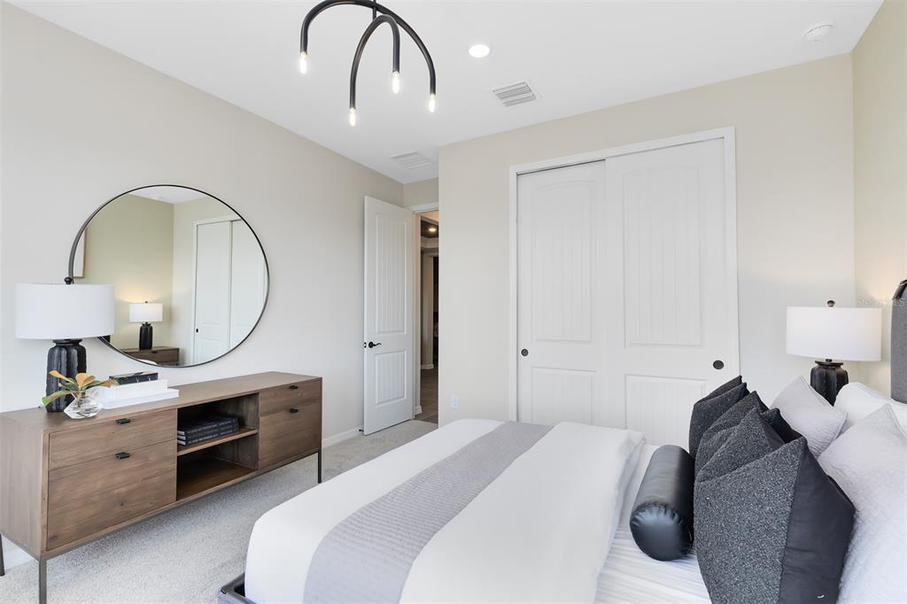 A bedroom features a bed, a wooden dresser with a round mirror, and sliding closet doors — 4620 SCENIC WOODS DRIVE, CLERMONT, FL