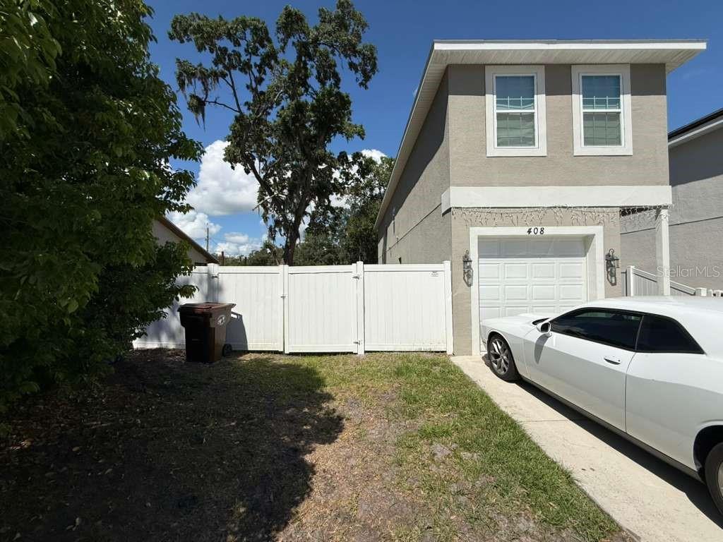 A two-story house with a white garage door, a white fence, and a parked car — 408 FINLEY AVENUE, KISSIMMEE, FL