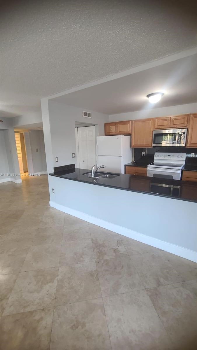 A kitchen features light wood cabinets, black countertops, a white refrigerator, and tile flooring — 16220 NW 2nd Ave # 213, Miami FL 33169, MIAMI, FL