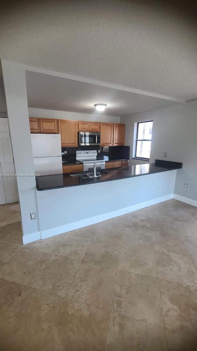 A kitchen with wood cabinets, black countertops, and a breakfast bar overlooking a tiled room — 16220 NW 2nd Ave # 213, Miami FL 33169, MIAMI, FL