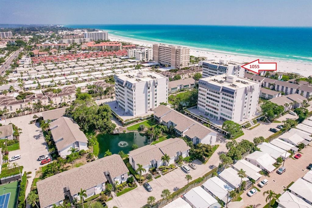 An aerial view shows two multi-story apartment buildings near a beach and a small pond — 1055 W PEPPERTREE DRIVE UNIT 603AA, SARASOTA, FL