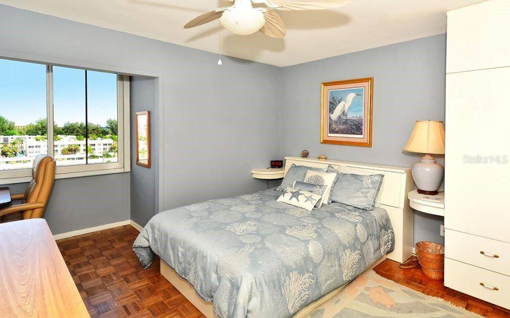 A bedroom features a bed with a patterned comforter, a ceiling fan, and large windows — 1055 W PEPPERTREE DRIVE UNIT 603AA, SARASOTA, FL