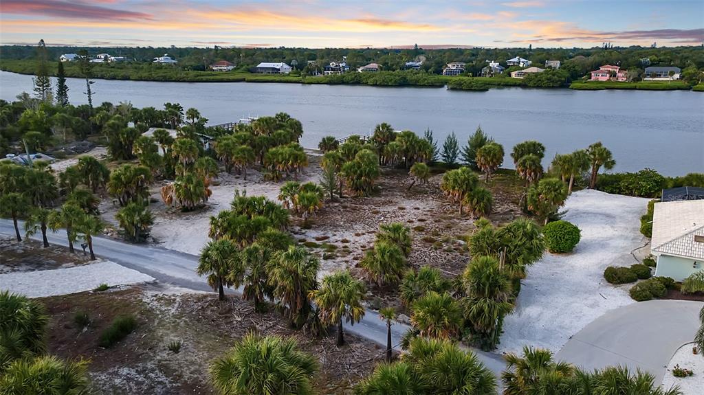 An aerial view shows a sandy, palm-filled vacant lot bordering a river at sunset — N MANASOTA KEY ROAD, ENGLEWOOD, FL