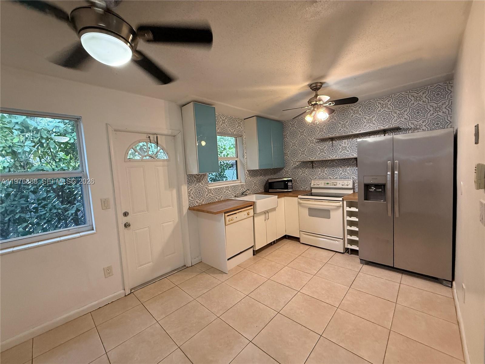 A kitchen features light blue upper cabinets, white lower cabinets, patterned wallpaper, and tile flooring — 1104 N 17th Ct # 105, Hollywood FL 33020, HOLLYWOOD, FL