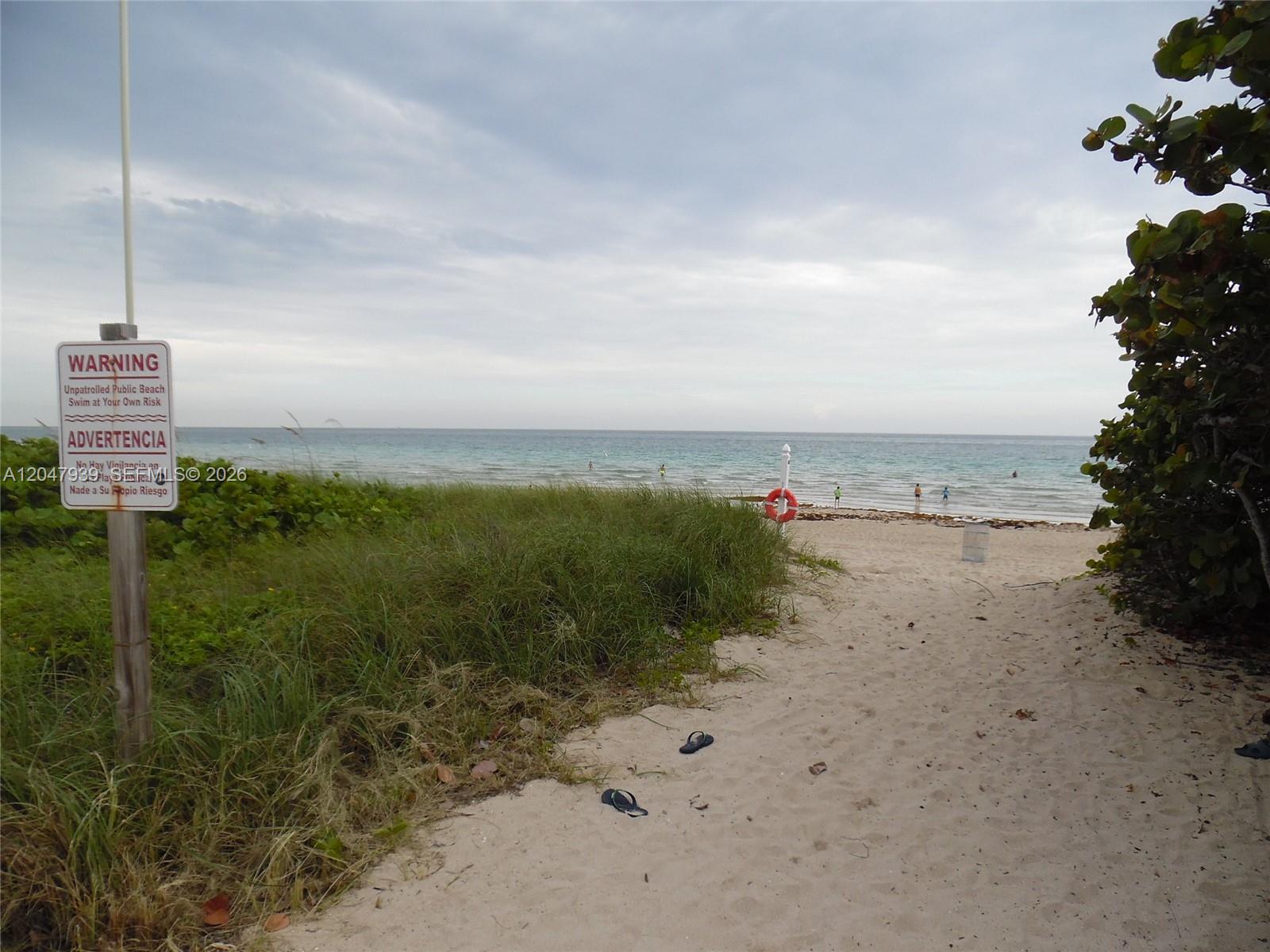 A sandy path leads through beach grass to the ocean with a warning sign nearby — 8911 Collins Ave # 1102, Surfside FL 33154, SURFSIDE, FL