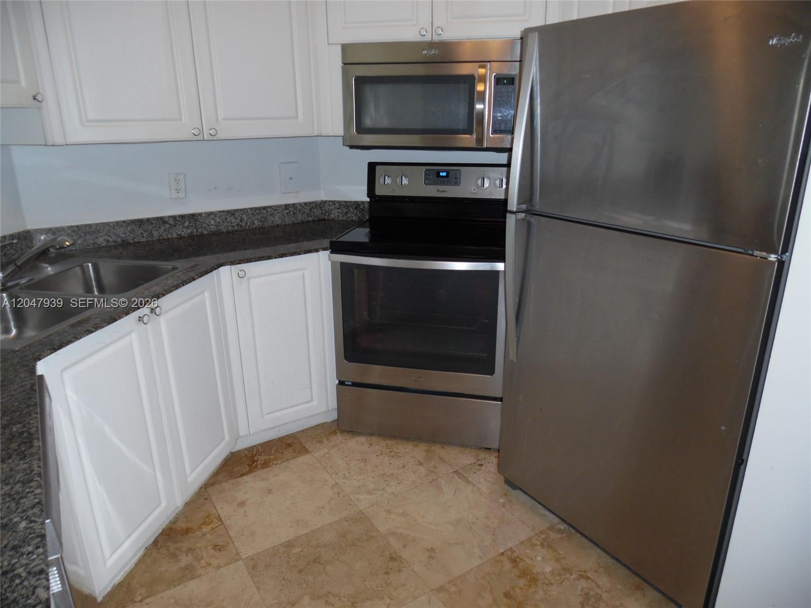 A kitchen features white cabinets, stainless steel appliances, granite countertops, and light-colored tile flooring — 8911 Collins Ave # 1102, Surfside FL 33154, SURFSIDE, FL