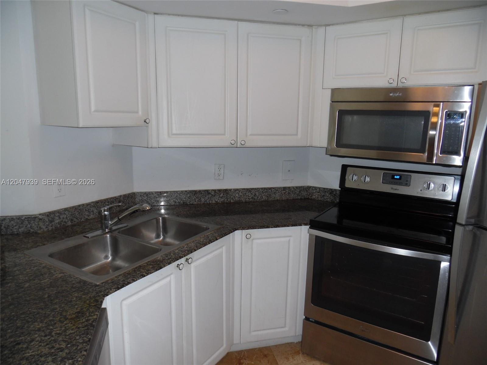 A kitchen features white cabinets, granite countertops, a stainless steel oven, and a microwave — 8911 Collins Ave # 1102, Surfside FL 33154, SURFSIDE, FL