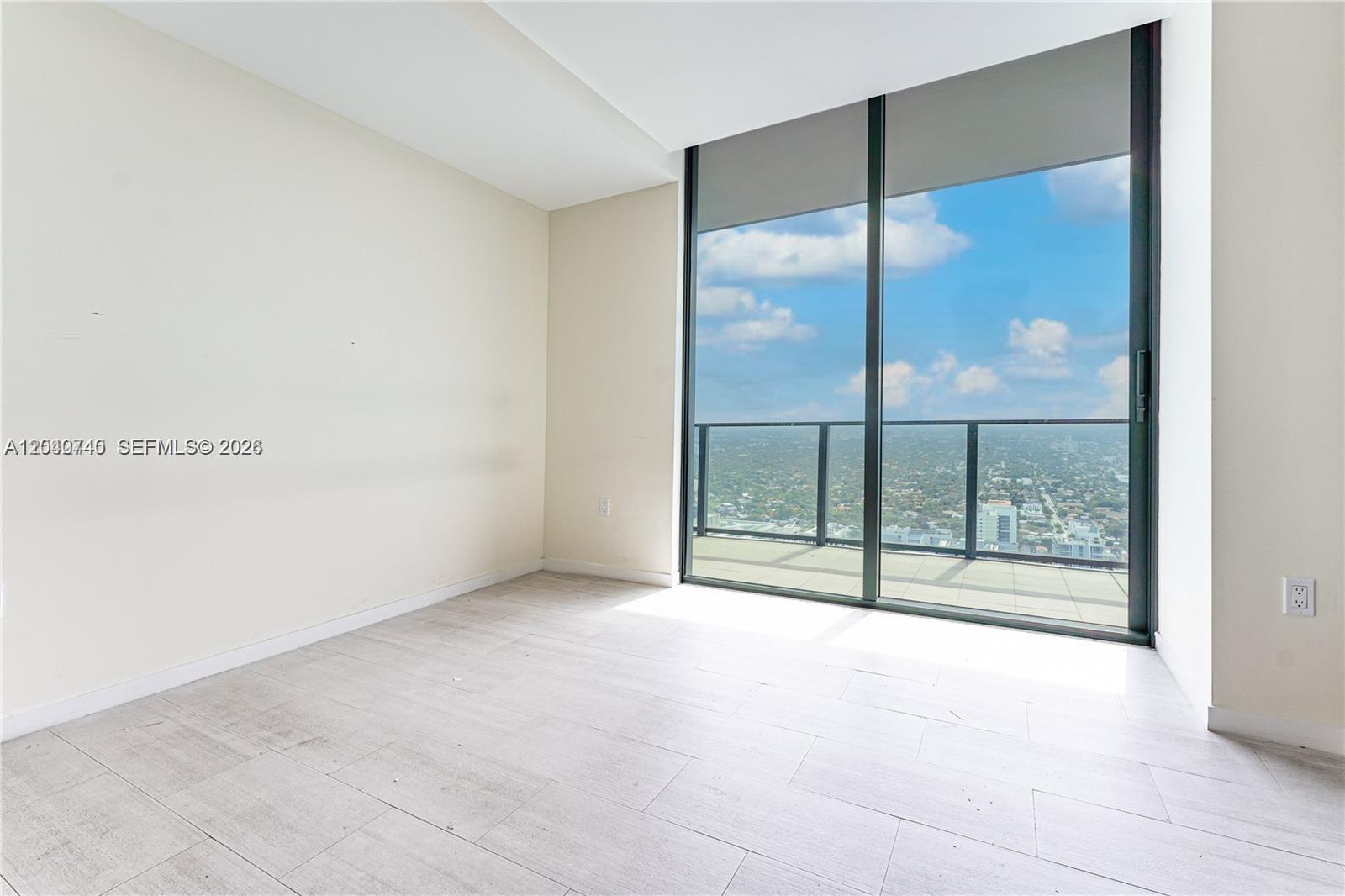 An empty room features light-colored tile flooring, white walls, and a large balcony glass door — 1000 Brickell Plz # 4906, Miami FL 33131, MIAMI, FL