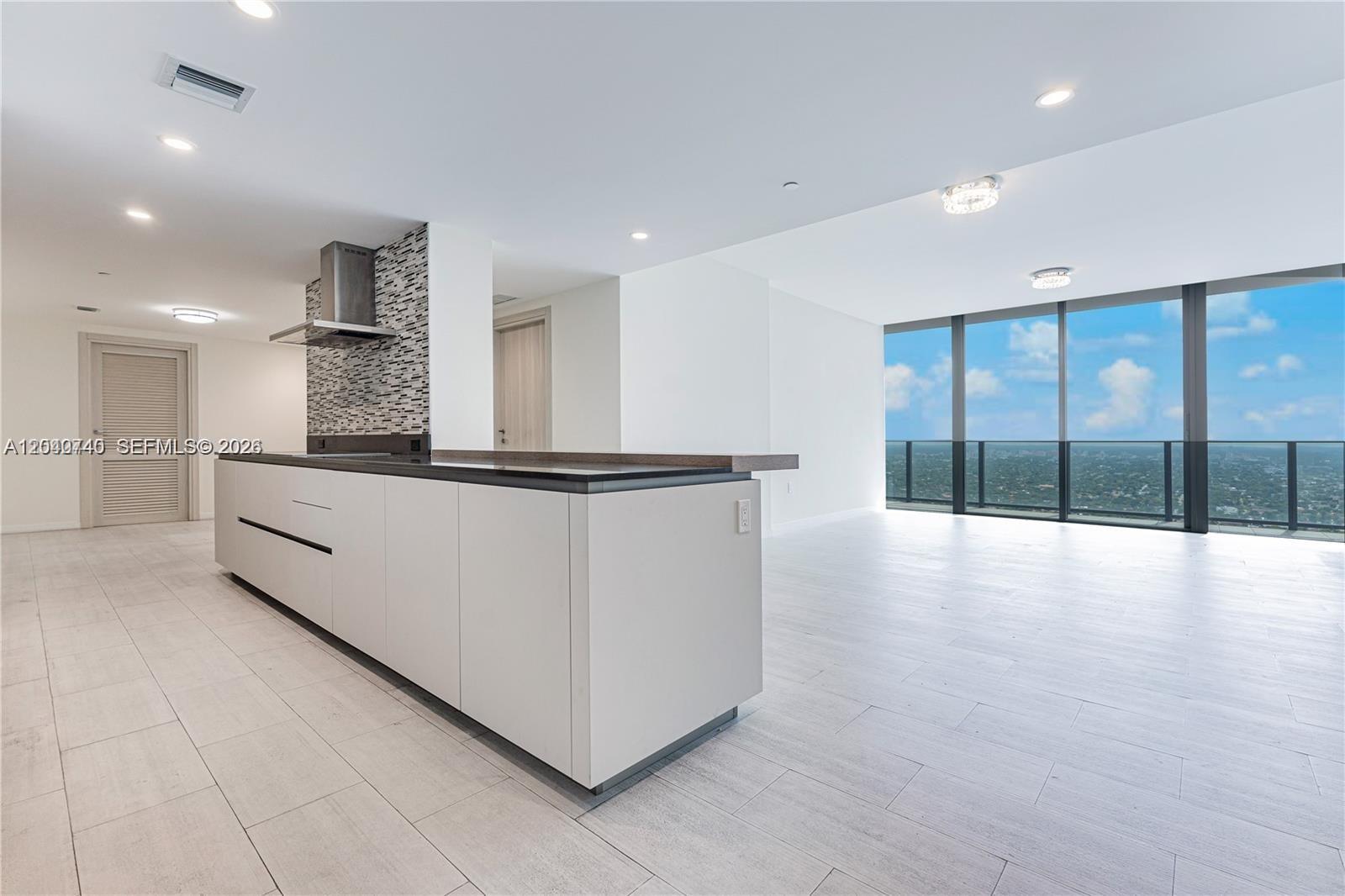 A modern kitchen with a large island and white cabinetry overlooks a city view — 1000 Brickell Plz # 4906, Miami FL 33131, MIAMI, FL